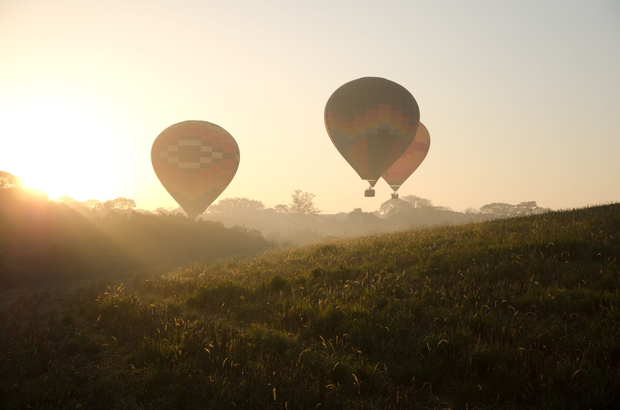 Three,Hot,Air,Balloons,Flying,Over,The,Hills,At,Sunrise